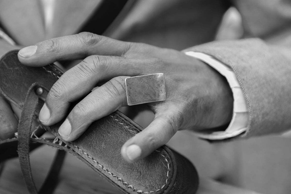 Main avec bague tenant une chaussure en cuir, atelier de cordonnerie Main avec bague tenant une chaussure en cuir, atelier de cordonnerie